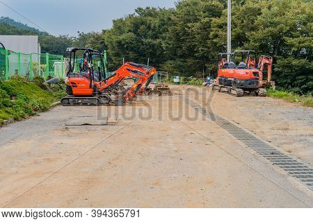 Chilgapsan, South Korea; September 30, 2020: Several Backhoes Sitting Idle N Parking Lot With Trees 