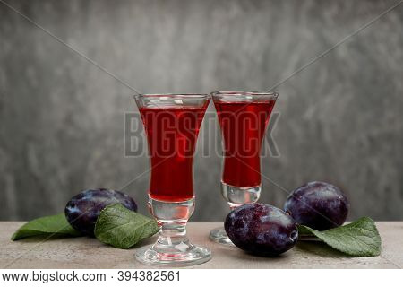 Delicious Plum Liquor And Ripe Fruits On Table Against Grey Background. Homemade Strong Alcoholic Be