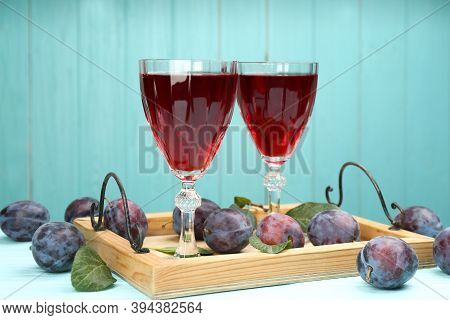 Delicious Plum Liquor And Ripe Fruits On Table Against Light Blue Background. Homemade Strong Alcoho