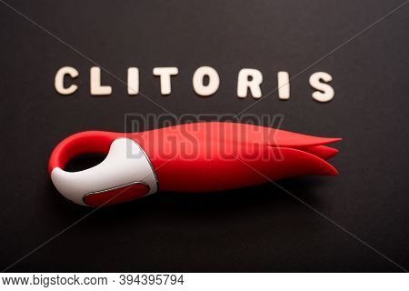 An Overhead View Of A Red Tulip Shaped Clitoral Vibrator And The Inscription Clitoris On A Black Bac