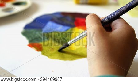 Close-up Of Childs Hand Drawn By Paintbrush And Gouache Color Circle On Sheet Of Paper. Children Cre
