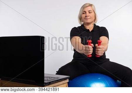 Senior Woman Doing Fitness Exercises With A Virtual Classroom Sitting On A Fitness Sword Holding Dum