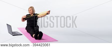 Banner, Long Format. Fitness At Home With A Trainer Online. An Elderly Woman Sits On A Mat In Front 