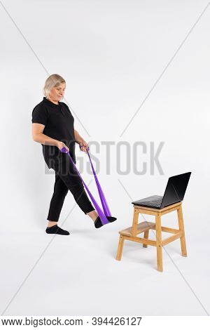 Gym At Home. Active Senior Woman Doing Leg Exercises Using Fitness Rubber Band At Home. Empty Space.