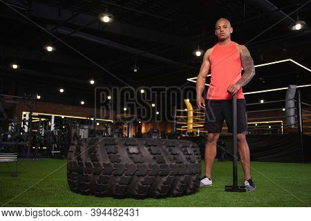 Low Angle Shot Of A Confident Strong African Sportsman Resting After Exercising With Sledgehammer. H