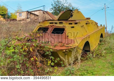 Side of an abandoned war tank with vegetation growing inside and some buildings in the backgrownd, close to Shushi in the Republic of Arstakh in Nagorno Karabakh