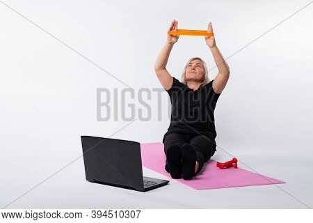 Online Senior Woman Workout With Elastic Band Sitting On Fitness Mat. Online Training Over The Inter