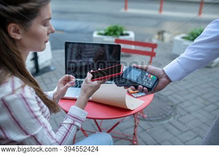 Brown-haired Female Paying Bill Through Payment Terminal In Open Air Cafe
