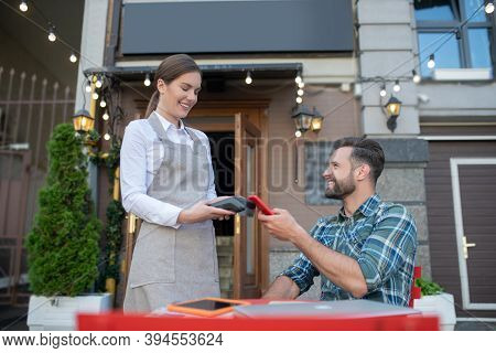 Bearded Male Paying Bill With Smartphone, Waitress Holding Payment Terminal