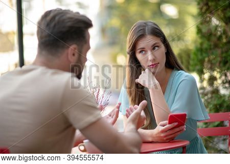 Couple Having Misunderstanding In Open Air Cafe, Sad Female Holding Her Phone