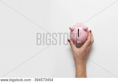 Womans Hand With Red Manicure Holds Money Piggy Bank On White Background With Copy Space. Save Money