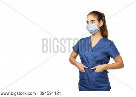Young Beautiful Female Doctor In A Blue Surgical Gown And A Medical Mask On Her Face Holds Her Hands