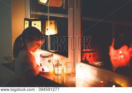 Little Kid Girl Sitting By Window With Selfmade Hand Crafted Lanterns With Candles For St. Martin Pr