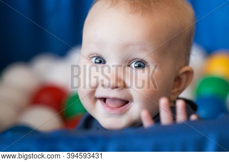 Cheerful Smiling Baby Girl With Blond Hair And Blue Eyes Sitting In The Ball Pit. Bright Colors Port