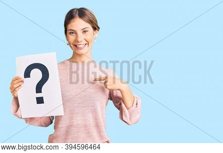 Beautiful caucasian woman with blonde hair holding question mark pointing finger to one self smiling happy and proud 