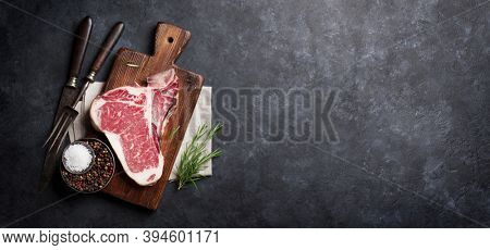 Raw T-bone steak cooking on wide stone table. Top view with copy space. Flat lay
