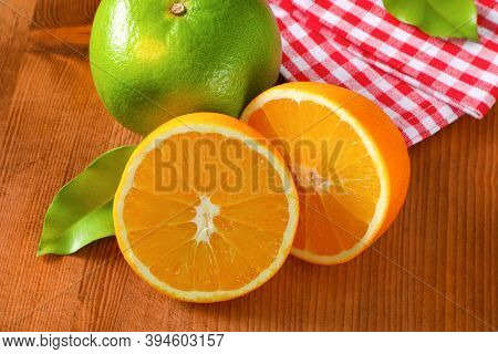 Green grapefruit (sweetie, pomelit, oroblanco), two orange halves and checked red and white tea towel on wooden table