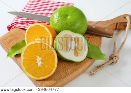Still life of green grapefruits (sweetie, pomelit, oroblanco grapefruit) and halved orange with knife and tea towel on cutting board