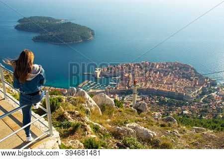 Attractive Brunette Traveller Sitting On A Railing Above The City Of Dubrovnik, Viewpoint On Srd Mou