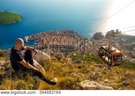 Wide Shot From The Top Of The Srd Mountain, Man Sitting On A Rock Observing The Area Around The City