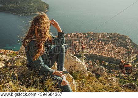Attractive Brunette Sitting On The Srd Hill Above The City Of Dubrovnik, Observing The City In The D