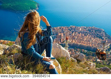 Attractive Brunette Sitting On The Srd Hill Above The City Of Dubrovnik, Observing The City In The D