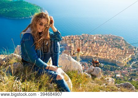 Attractive Brunette Sitting On The Srd Hill Above The City Of Dubrovnik, Observing The City In The D
