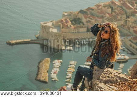 Attractive Brunette Seen From Behind Posing While Sitting On A Stone Above The City Of Dubrovnik, Ou