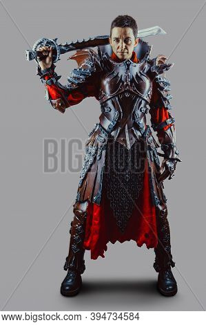 Portrait Of A Medieval Female Knight In Armor With A Sword In Hand. Isolated Over Grey Background.