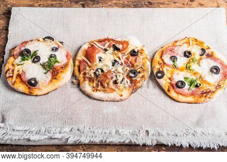 Several Ready-made Mini Pizza, Pizzetta With Sausage And Bacon, Jamon On A Linen Napkin On A Wooden 