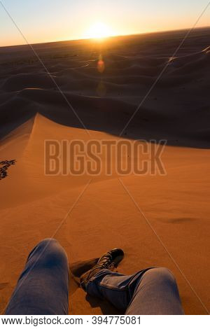 Legs Of Unrecognizable Man From The Top Of A Dune At Sunrise, In Erg Chigaga, Morocco