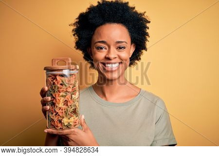 Young African American afro woman with curly hair holding bottle of dry Italian pasta with a happy face standing and smiling with a confident smile showing teeth