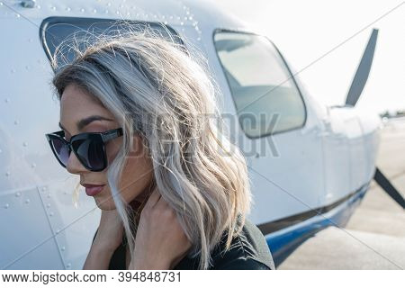 A gorgeous young blonde model poses outdoors with a single engine aircraft at a local airport