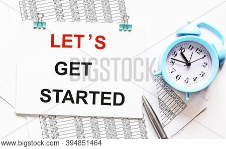 Notepad With The Text Let's Start, Isolated On Papers With Numbers, Near A Pen And An Alarm Clock On