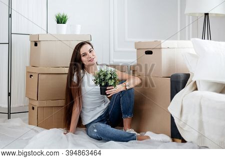 Young Woman With A Home Plant Sitting On The Floor In The New L