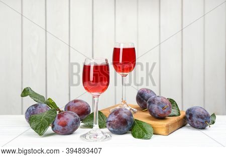 Delicious Plum Liquor And Ripe Fruits On Table Against White Background. Homemade Strong Alcoholic B