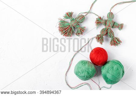 Handmade Dolls Of Red And Green Threads On The White Table. Martenichki, Slavic Mascots Symbolising 