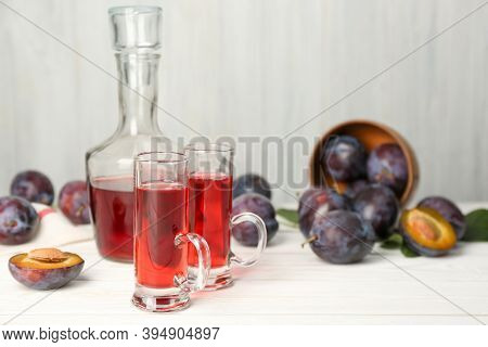 Delicious Plum Liquor And Ripe Fruits On White Wooden Table, Space For Text. Homemade Strong Alcohol