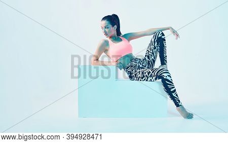 Sporty Fit Girl In Stylish Sportswear Sitting On Cube In Neon Studio Light. Perfect Body Shapes. Hea