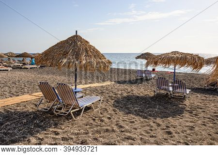Santorini, Greece - September 16, 2020: Straw Umbrellas With Sun Loungers At The Vlychada Beach On T