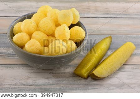 Dill Pickle Corn Puffs In Snack Bowl With Dill Pickle Spears In Table