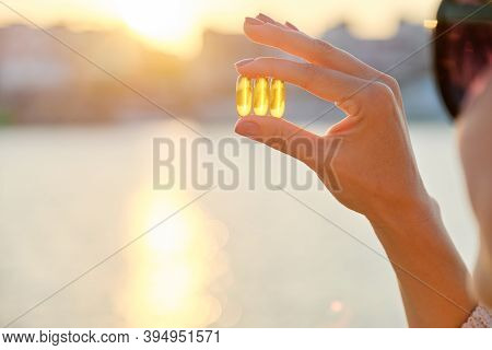 Yellow Gel Capsule Vitamin D Omega-3 In Womans Hand, Sun Sea Background.