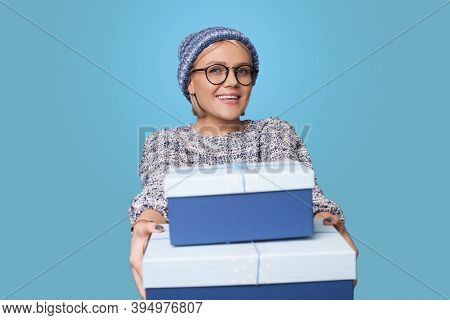 Blonde Woman With Hat And Glasses Is Receiving Present At The Holiday Smiling On A Blue Studio Wall 