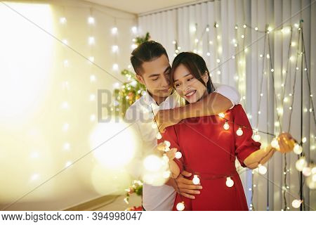 Beautiful Young Couple In Love Standing In Living Room Tangled In Christmas Lights