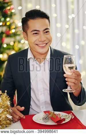 Portrait Of Smiling Guest Telling Toast At Christmas Dinner And Raising Hand With Glass Of Champagne