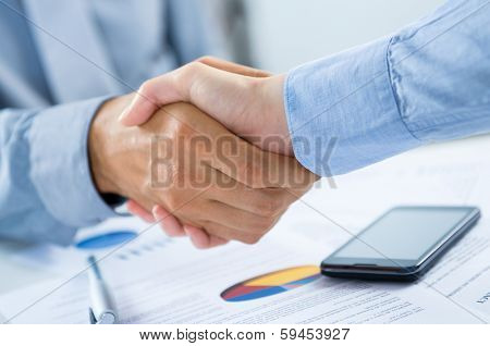Close Up Of Businesspeople Shaking Hands At Desk