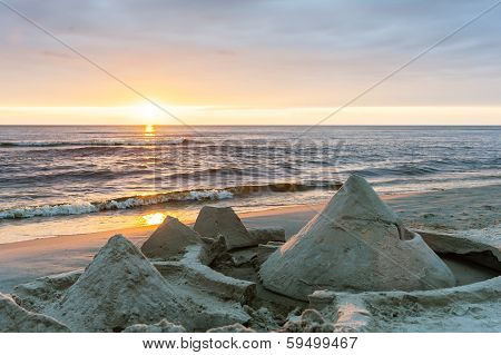 Sandcastles Built On The Beach By The Sea With Sunset In The Back.