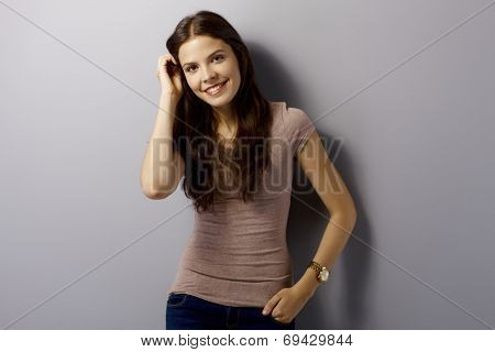 Portrait of happy young woman standing by grey wall, smiling, looking at camera.