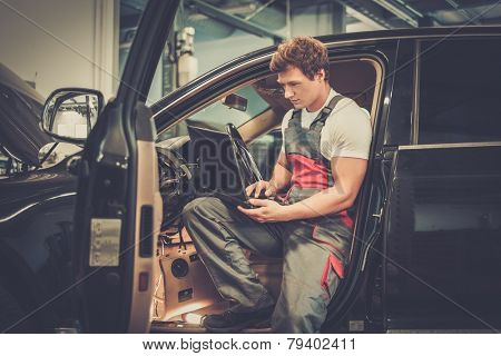 Serviceman making car diagnostics with laptop in a workshop
