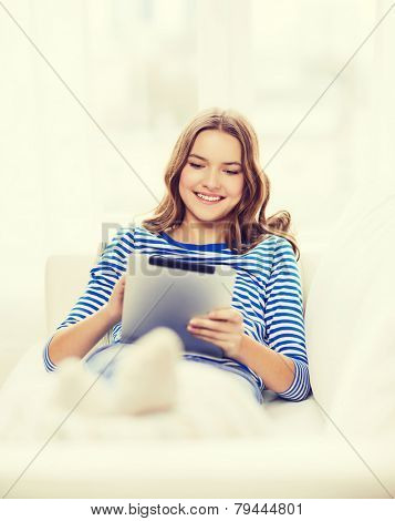 home, technology and internet concept - smiling teenge girl lying on the couch with tablet pc computer at home